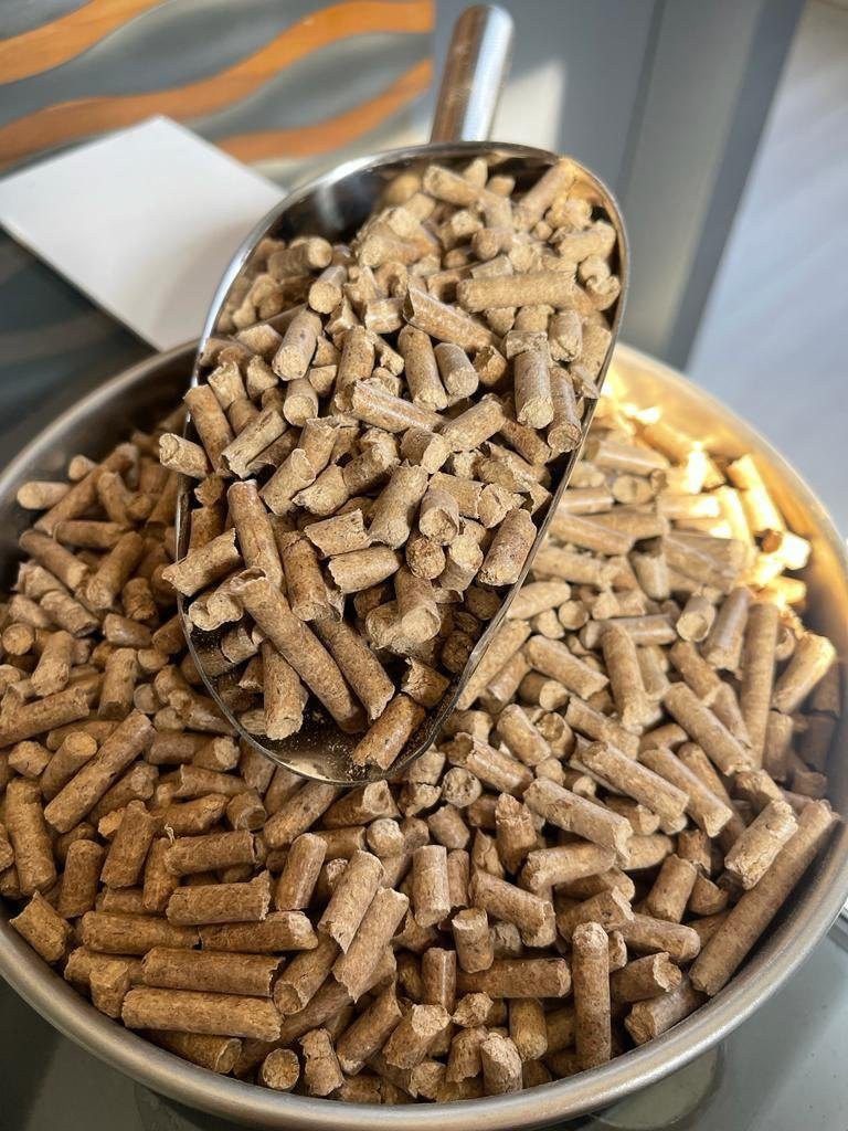Freshly produced pine pellets in a metal scoop next to stacked pallets in the warehouse